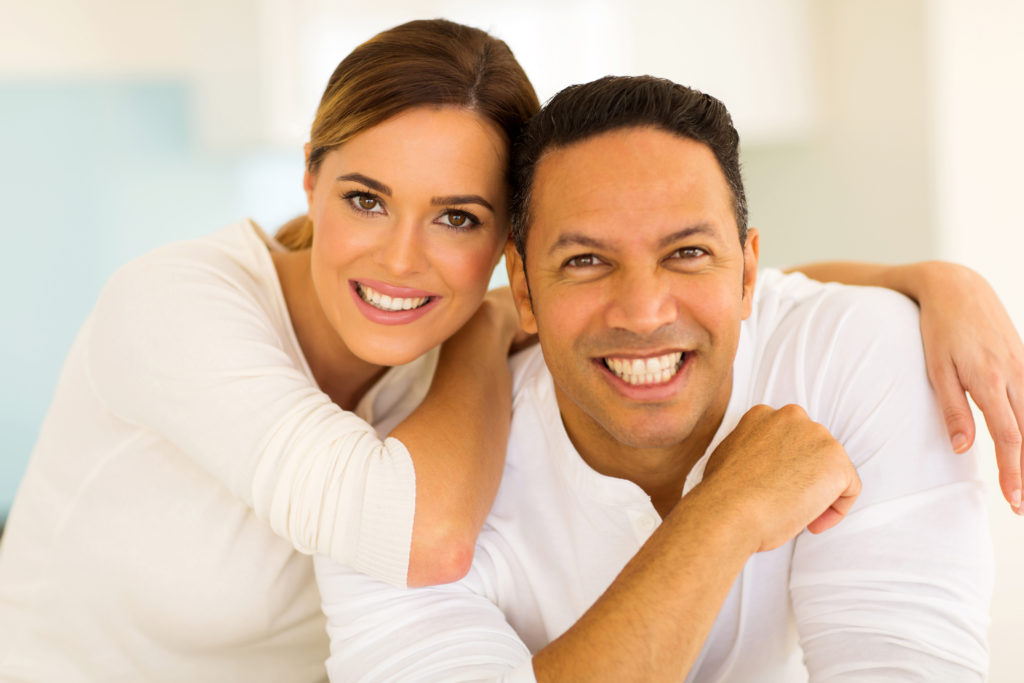 Young couple smiling and showing off their results from teeth whitening treatment. 